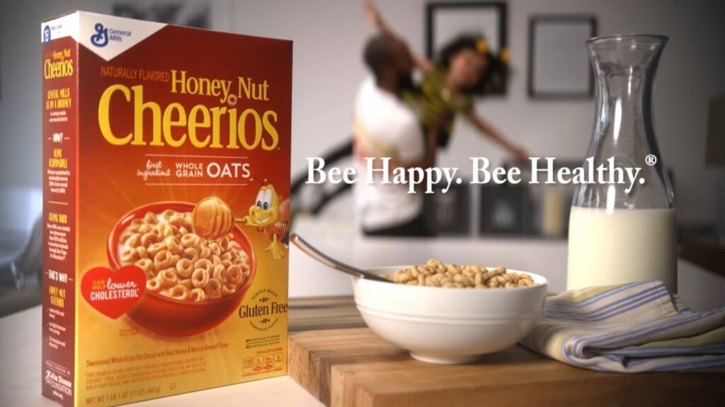 food and beverage slogans bee happy, bee healthy cereal in foreground, father and daughter playing in the background